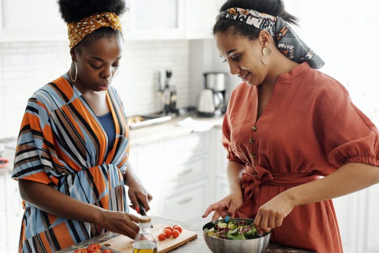 Two women of color preparing a healthy salad with fresh ingredients on a cutting board