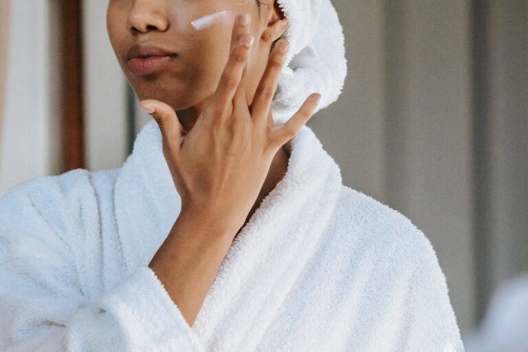 Close-up of a woman applying cosmetic cream on her face with her fingers.