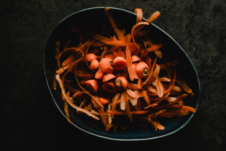 Fresh carrots being peeled in a bowl.