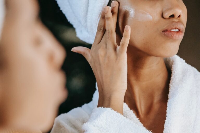 Close-up shot of an ethnic woman applying cream on her face while looking at herself in the mirror.